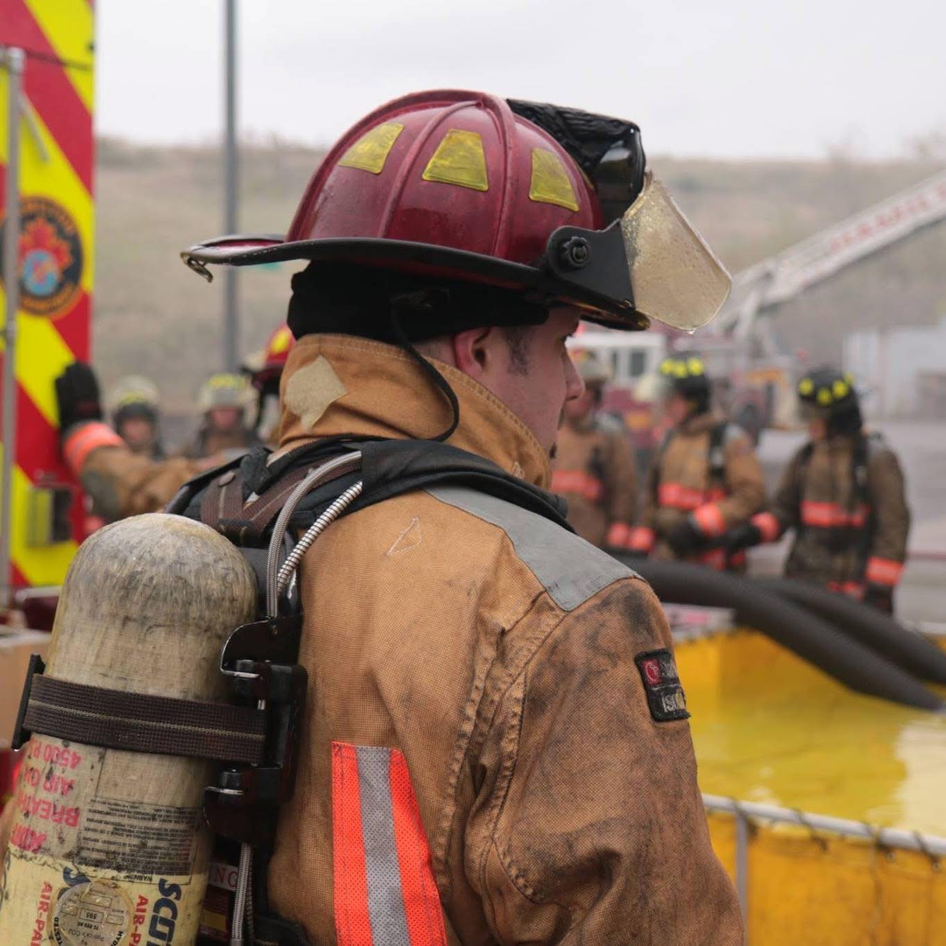 A fire instructor in full bunker gear supervises a rural water supply training session for new recruits in Hamilton, Ontario.